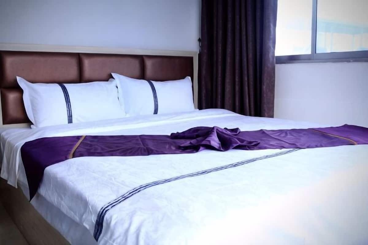 Habitación de hotel con cama, cabecero y ventana con cortinas.