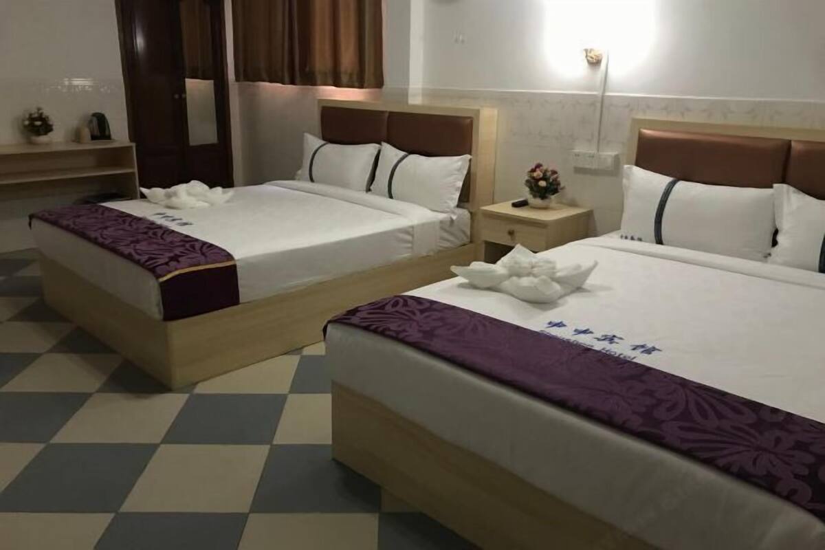 Habitación de hotel con dos camas, una mesita de noche, una lámpara y piso a cuadros.