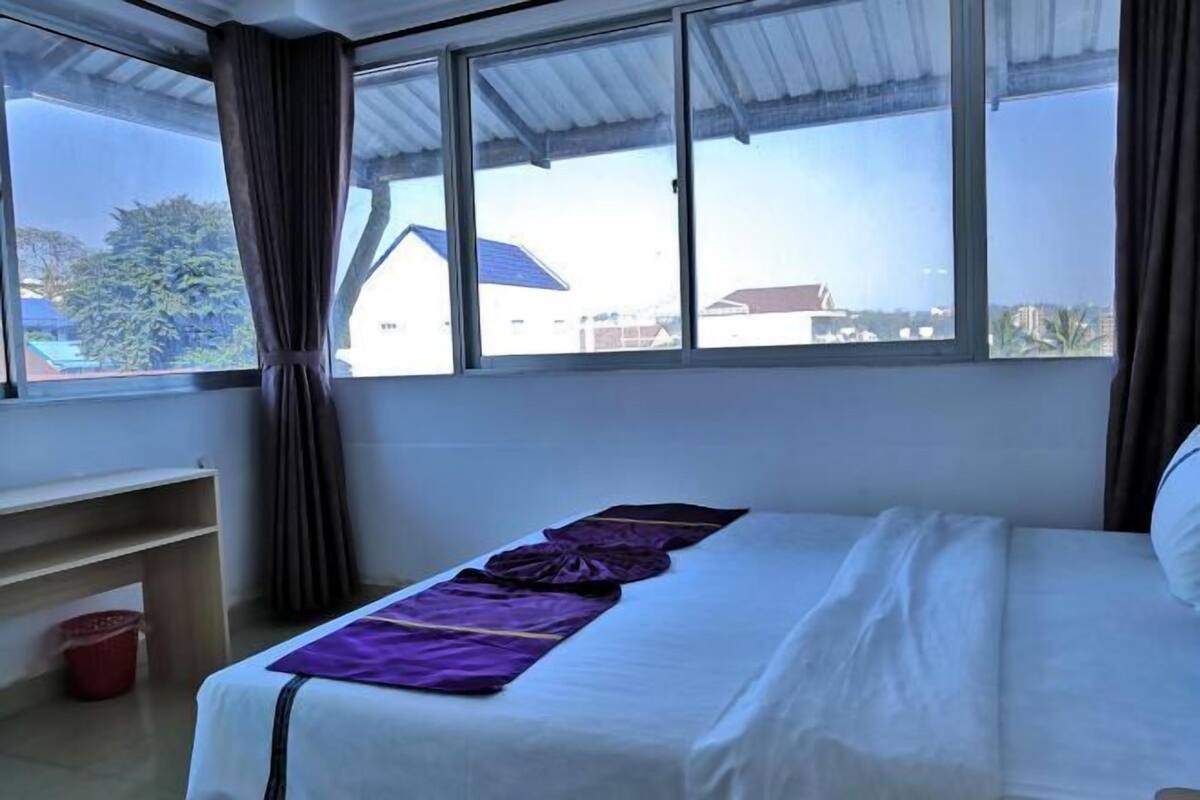 Una habitación con cama, ventana y vistas a edificios y árboles.