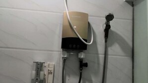 A shower with a handheld showerhead, a control panel, and a water inlet.