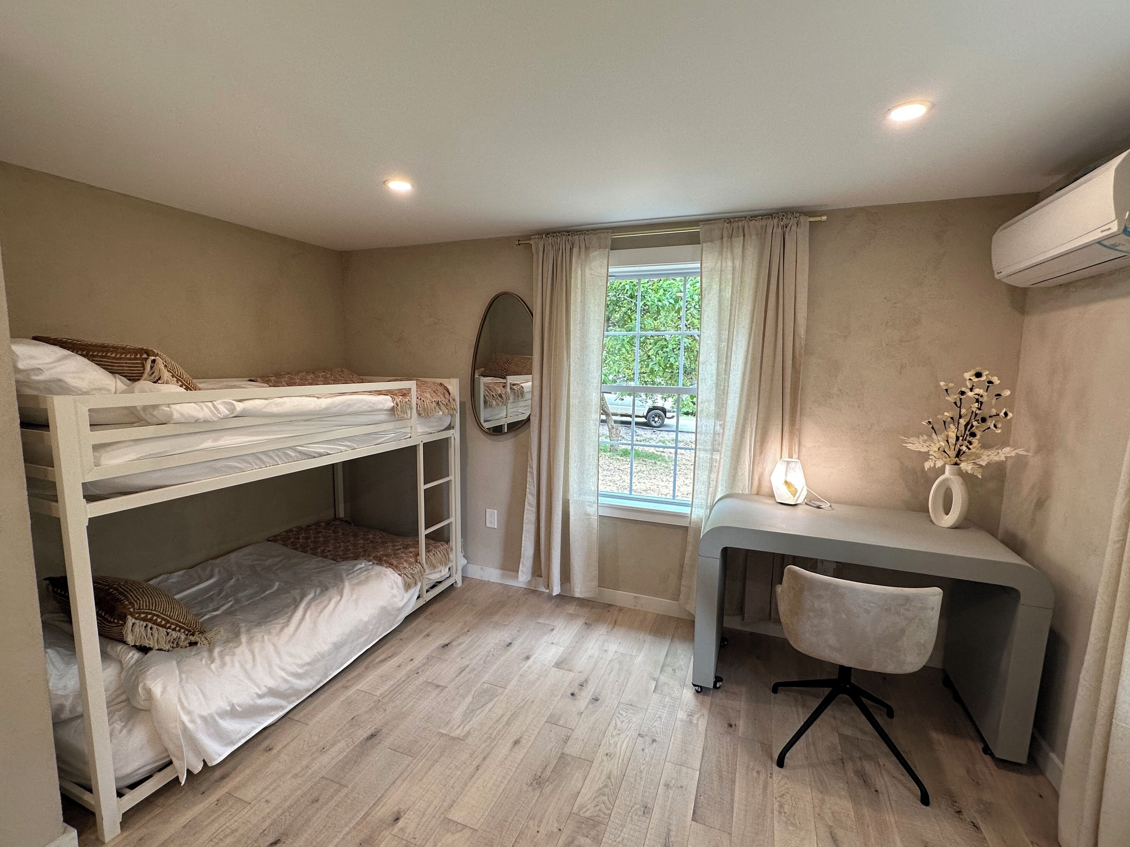 A bedroom with bunk beds, a desk, a chair, a mirror, and a window with curtains.