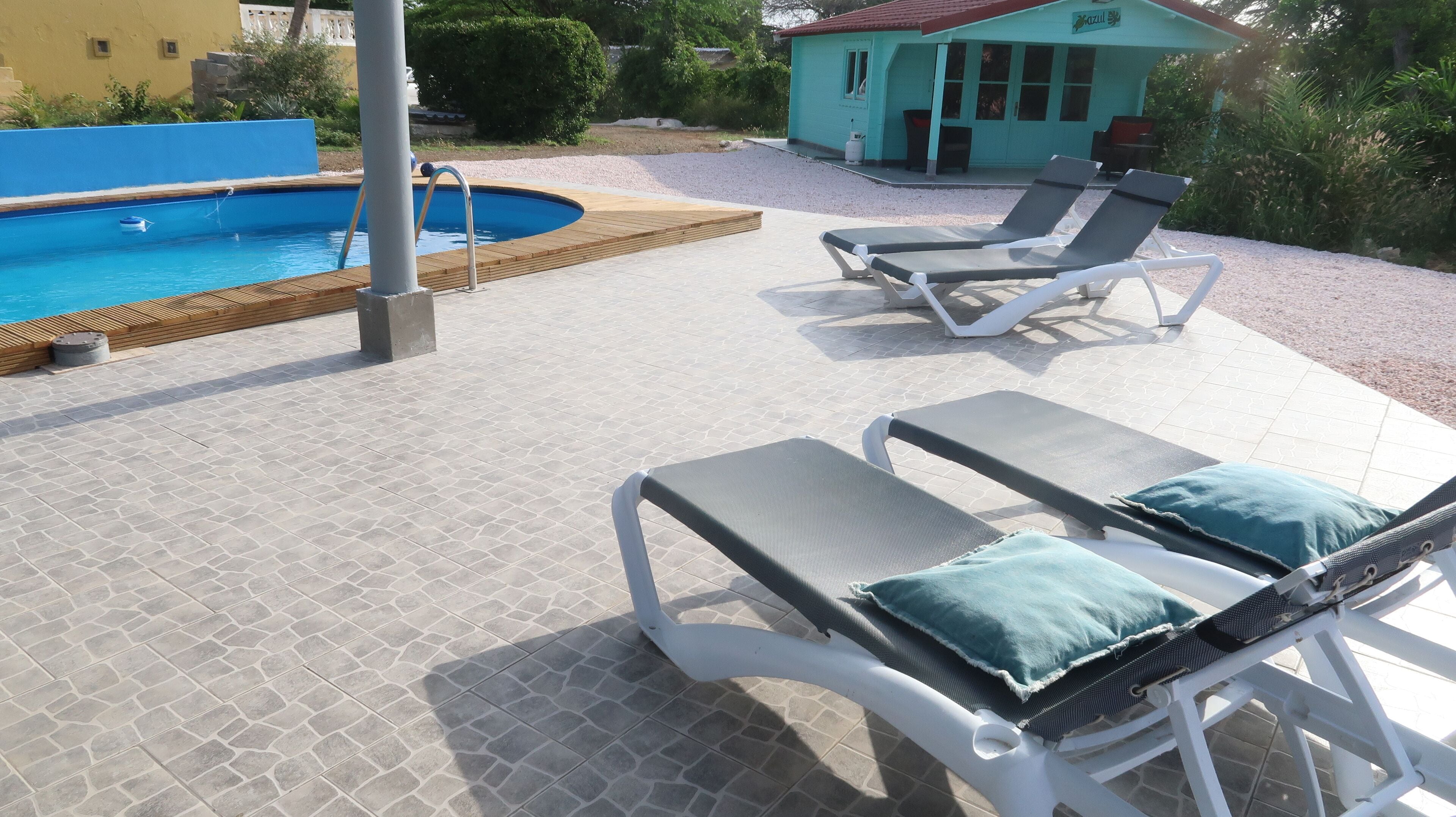 A pool area with two lounge chairs and a small building in the background.
