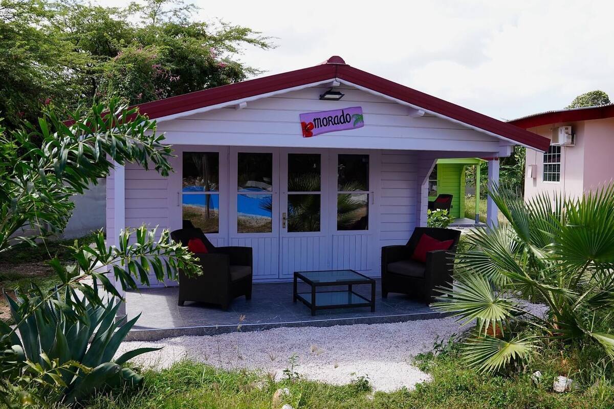 A small, single-story building with a red roof and a sign that reads "morado". It features a covered outdoor seating area with two chairs and a table.