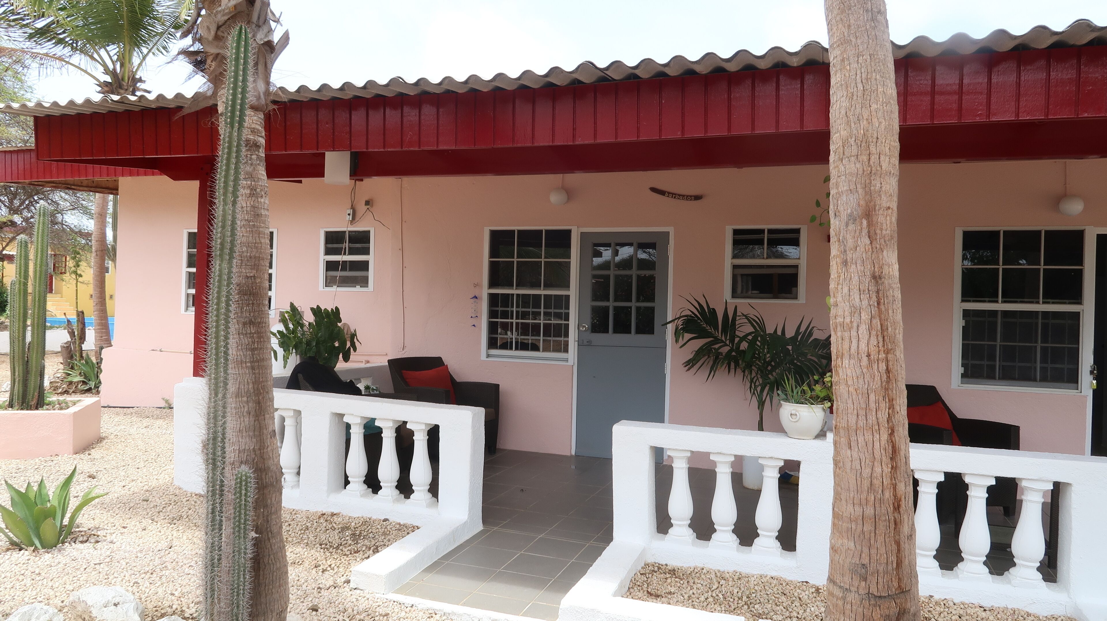 Una casa con techo rojo, un porche con barandas blancas y una puerta que dice 'barbados'.