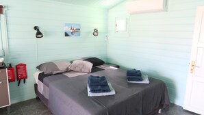 Una habitación con cama, dos mesitas de noche, una lámpara de pared, un extintor y una ventana.