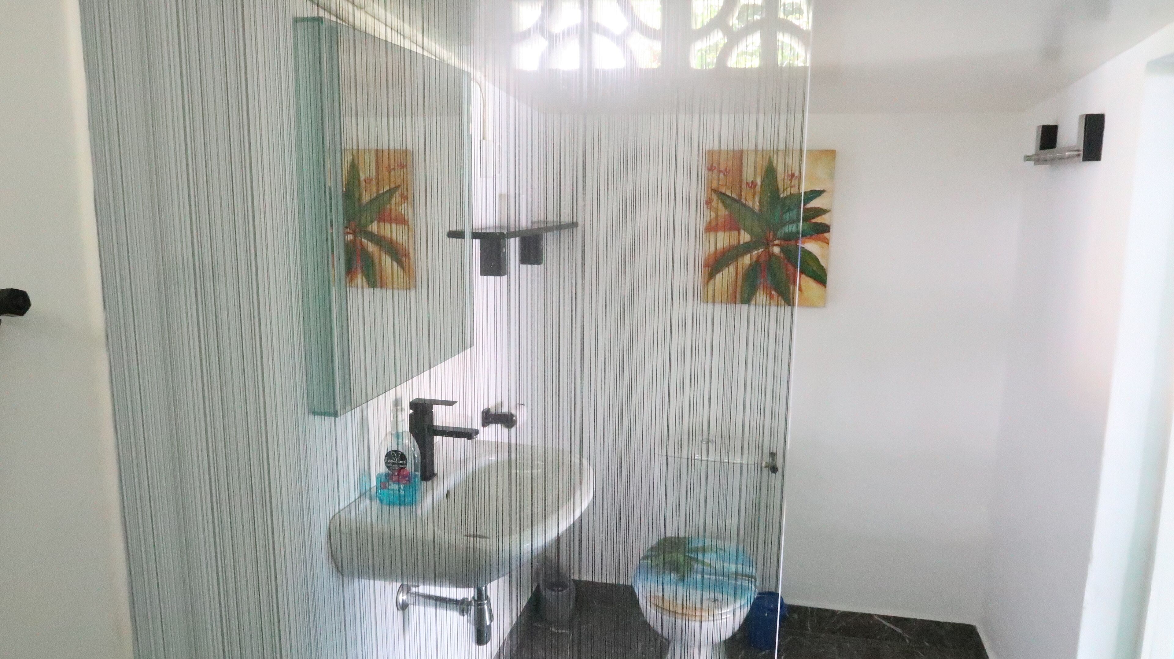 Un baño con mampara de vidrio, lavamanos, espejo y dos toalleros de pared.