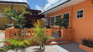A building with a yellow facade, multiple windows, and a covered patio area with potted plants.
