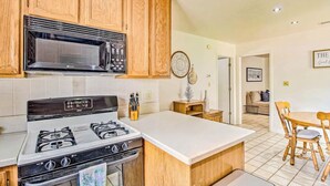 A kitchen with wooden cabinets, a microwave, a gas stove, and a dining area with a wooden table and chairs. - Cozy Cottage in the Heart of Lakeside (Lakeside)