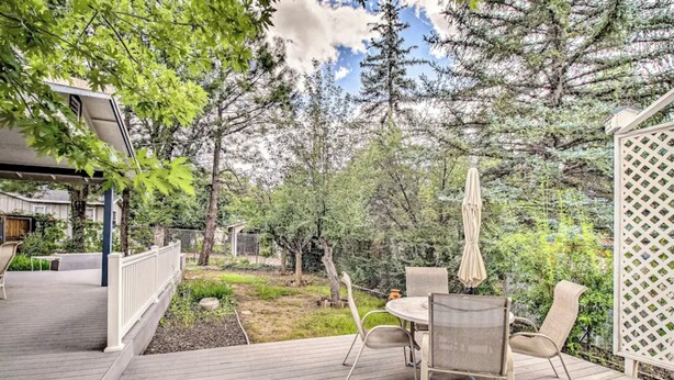 A wooden deck with outdoor furniture, including a table and chairs, surrounded by trees and a fence. - Cozy Cottage in the Heart of Lakeside (Lakeside)