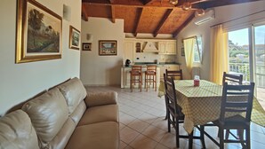 Uma sala de estar aconchegante com um sofá de couro, uma área de jantar com toalha quadriculada e uma cozinha com armários brancos.