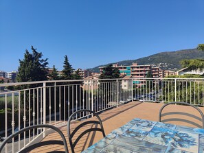A terrace with a table and chairs, overlooking a residential area with buildings and a hill in the background. - Terrace Apartment by Tempovacanza (Marina di Andora)