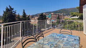 Uma varanda com mesa e cadeiras, com vista para uma área residencial com edifícios e árvores.