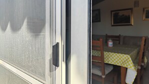 Um quarto com uma mesa de jantar coberta por um tecido xadrez amarelo e branco, cadeiras de madeira e uma parede branca com quadros.