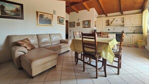 Uma sala de estar aconchegante com um sofá de couro, uma mesa de jantar com cadeiras e uma cozinha com armários brancos e piso ladrilhado.
