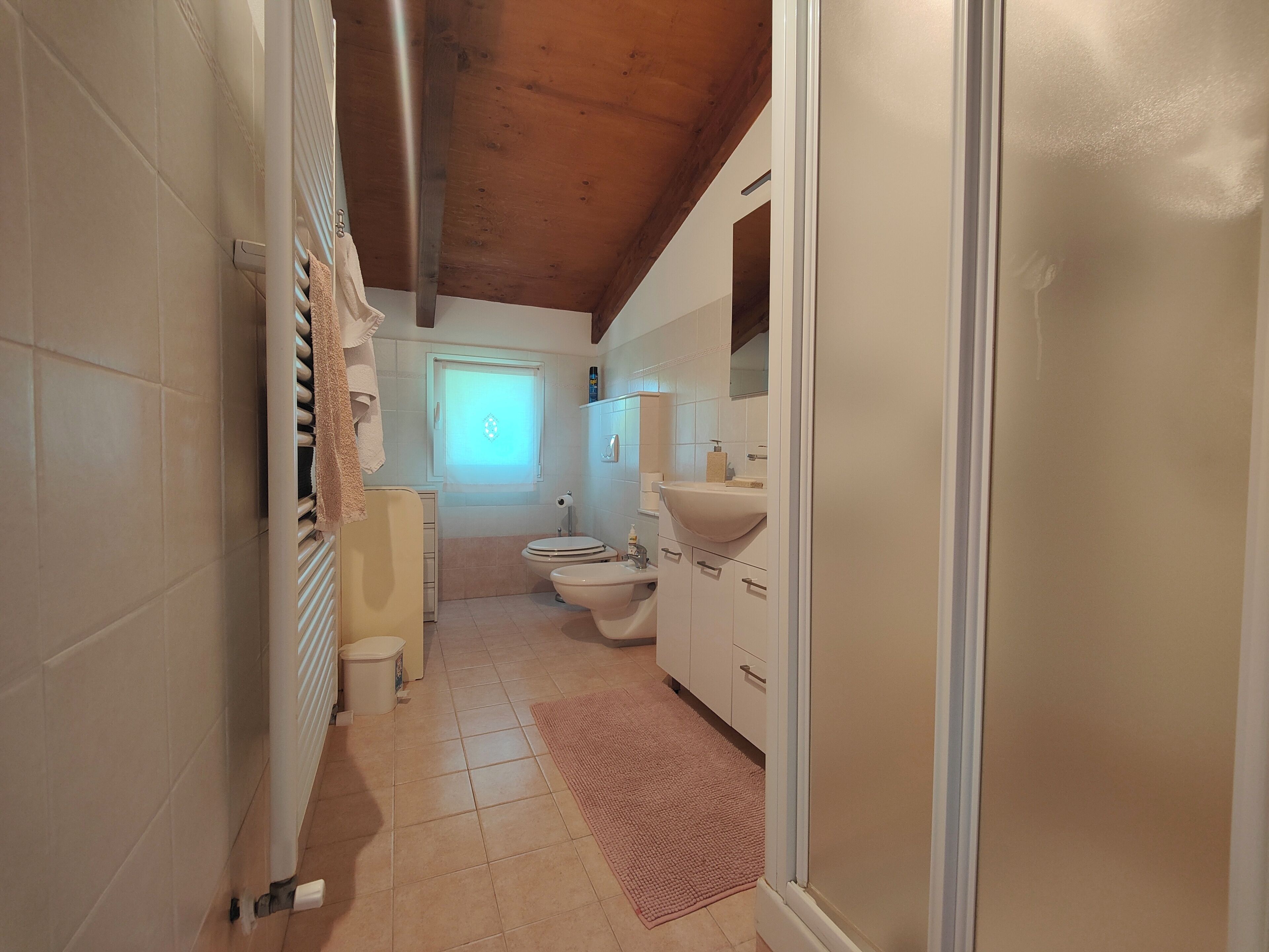 A narrow bathroom with a toilet, sink, and window.