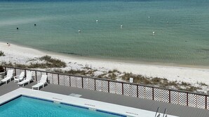 A pool with clear blue water, a sandy beach, and a view of the ocean.