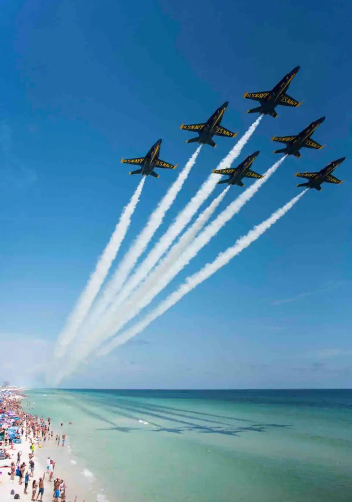 A beach with a crowd of people and a group of jets performing an aerial maneuver.