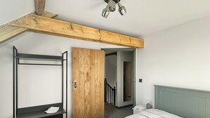 Une chambre avec un lit superposé, une armoire en bois, un petit bureau et un lit recouvert d’une couette blanche.