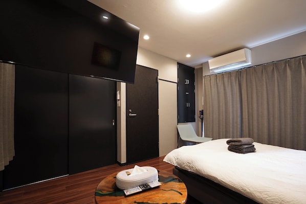 Et moderne hotelværelse med en seng, et rundt træbord med håndklæde og servietter, en mørk garderobe, et spejl og en aircondition.