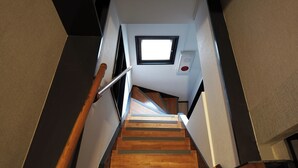 A wooden staircase with a handrail, a small window at the top, and a fire alarm on the wall.