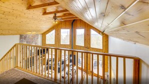 Un interior de madera con una escalera que conduce a un nivel superior, paredes de piedra y ventanas amplias.