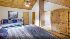 Un dormitorio con cama, ventilador de techo, armarios de madera y un cuadro en la pared.