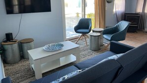Un soggiorno con una grande TV a schermo piatto montata a parete, un divano grigio, due poltrone blu, un tavolino da caffè bianco e una ciotola decorativa.