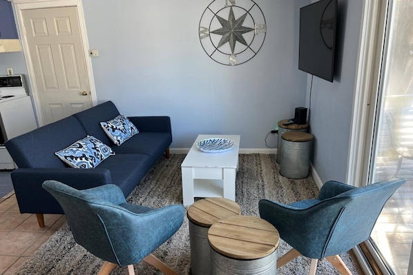 A living room with a sofa, two chairs, a small table, a decorative compass wall art, a TV, and a window with a view. - Sunnyside (Newbury)