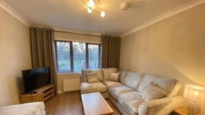 A cozy living room with a sofa, a coffee table, a TV, and a lamp. - DiscoverNESS Apartment (Inverness)