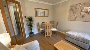 A living room with a sofa, a coffee table, a dining table with chairs, a potted plant, and a world map on the wall. - DiscoverNESS Apartment (Inverness)
