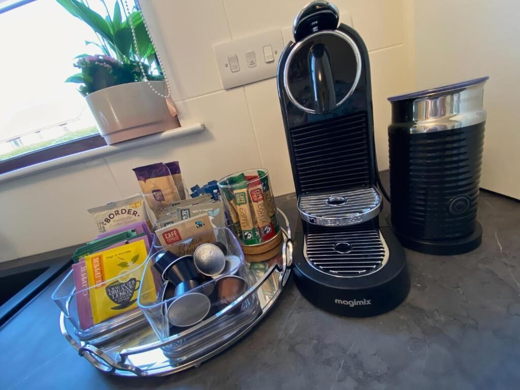 Une cuisine équipée d’une machine à café, d’un plateau avec des capsules de café et des tasses, et d’une plante en pot.