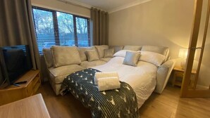 A bedroom with a large bed, a sofa bed, a TV, and a bedside table. - DiscoverNESS Apartment (Inverness)