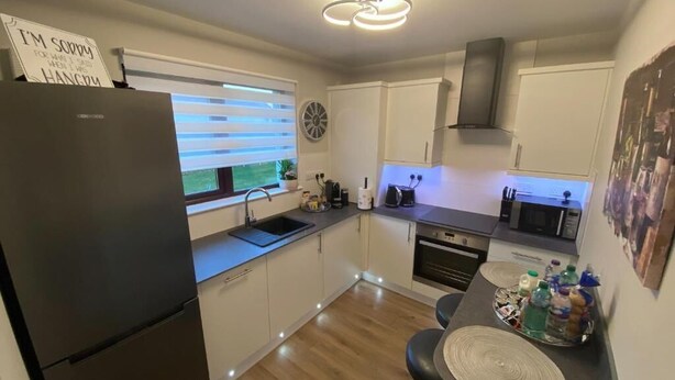 A compact kitchen with a refrigerator, sink, and dining area. - DiscoverNESS Apartment (Inverness)