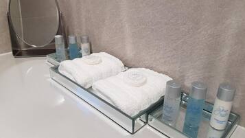 A bathroom vanity with a glass tray holding two white towels, a round mirror, and several bottles of spa products.
