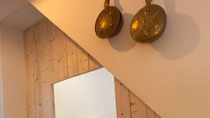 Quarto com teto inclinado de madeira, cama com roupa de cama branca, luminária de cabeceira e espelho refletindo o quarto.