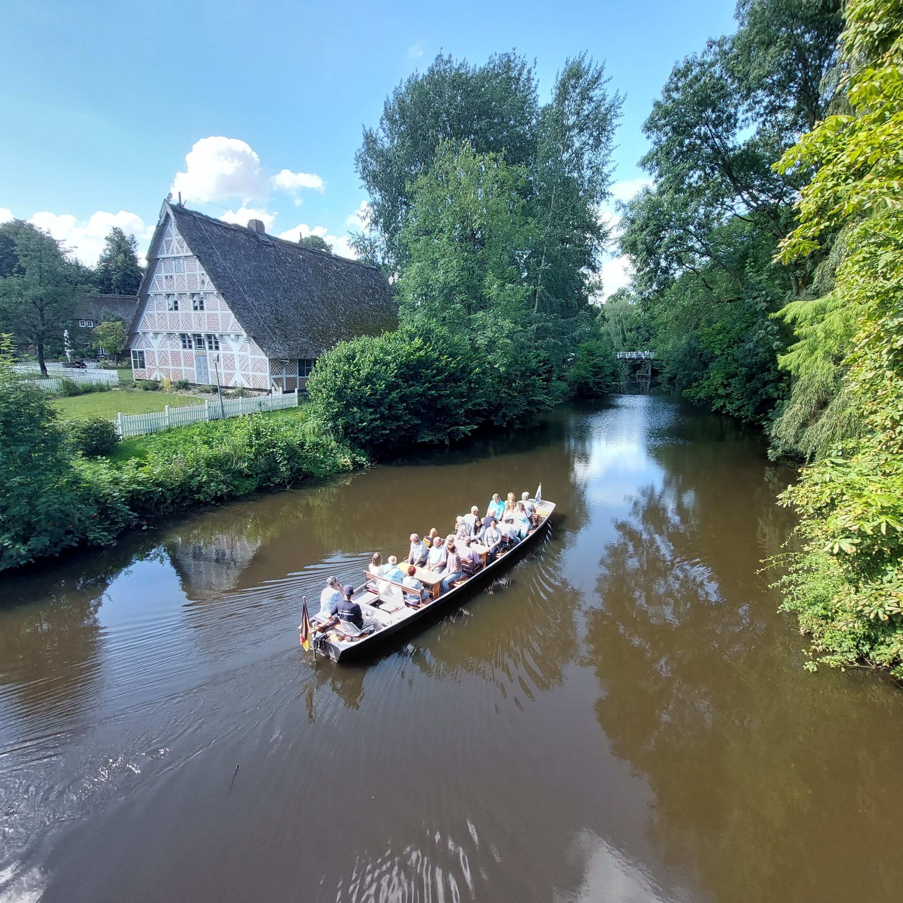 Un bote con pasajeros en un río tranquilo, rodeado de exuberante vegetación y una edificación tradicional con techo de paja.