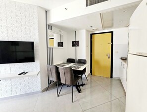 A modern kitchen with a dining area, a flat-screen TV mounted on the wall, a yellow door, and a refrigerator. - 908 (Bat Yam)