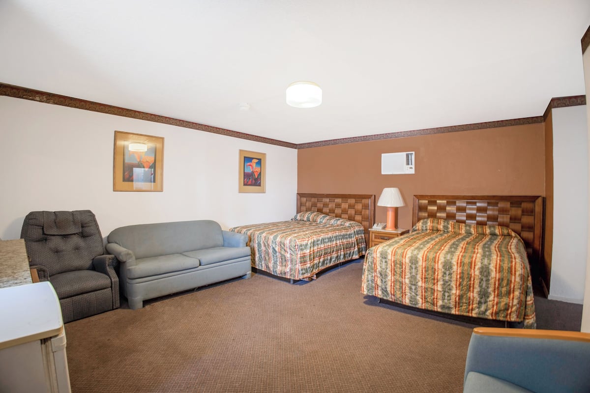 A hotel room with two single beds, a sofa, a chair, and a small table.