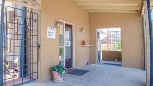A hotel entrance with a metal gate, a door with a sign, a potted plant, and a small shelf with a red object. - Sands Motel By OYO El Paso Near Airport (El Paso)