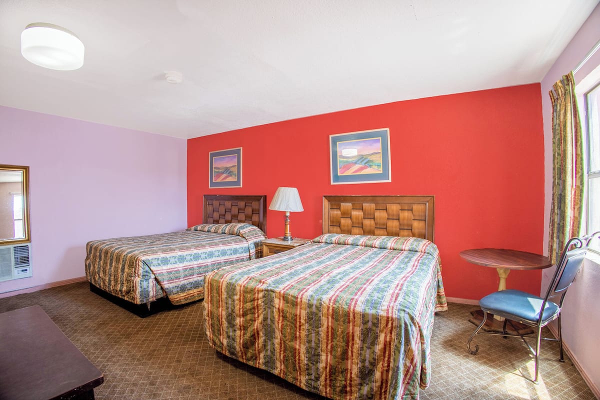 A hotel room with two beds, a small table, a chair, and a window with curtains.