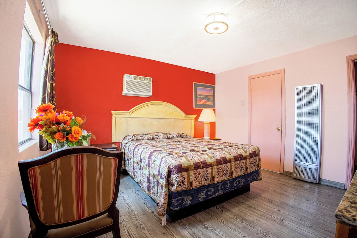 A room with a bed, a chair, a window with curtains, a wall-mounted air conditioner, and a door.