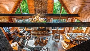 Ein großzügiger Loft-Wohnbereich mit Kamin aus Stein, Ledermöbeln und großen Fenstern mit Blick ins Freie.