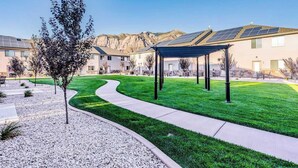 A residential area with a covered outdoor seating area, a well-maintained lawn, and a building with solar panels. - 30% OFF PROMO! East Ogden Dream, Newly Built, BBQ, Patio, Views, Dedicated Spa! (Ogden)