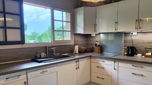 Une cuisine moderne avec des meubles blancs, un lave-vaisselle Bosch, une grande fenêtre et un luminaire suspendu.