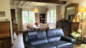 Un salon chaleureux avec un canapé en cuir noir, une table à manger avec des chaises, une bibliothèque et un grand miroir.