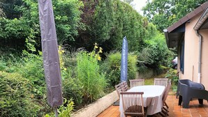 Une terrasse extérieure avec une table ronde et des chaises, entourée de verdure et dotée d’un sol carrelé.