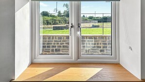 Ein Zimmer mit Blick auf ein grünes Feld und eine Steinmauer, sichtbar durch doppelte Türen mit Holzrahmen und einem grünen Rollvorhang.