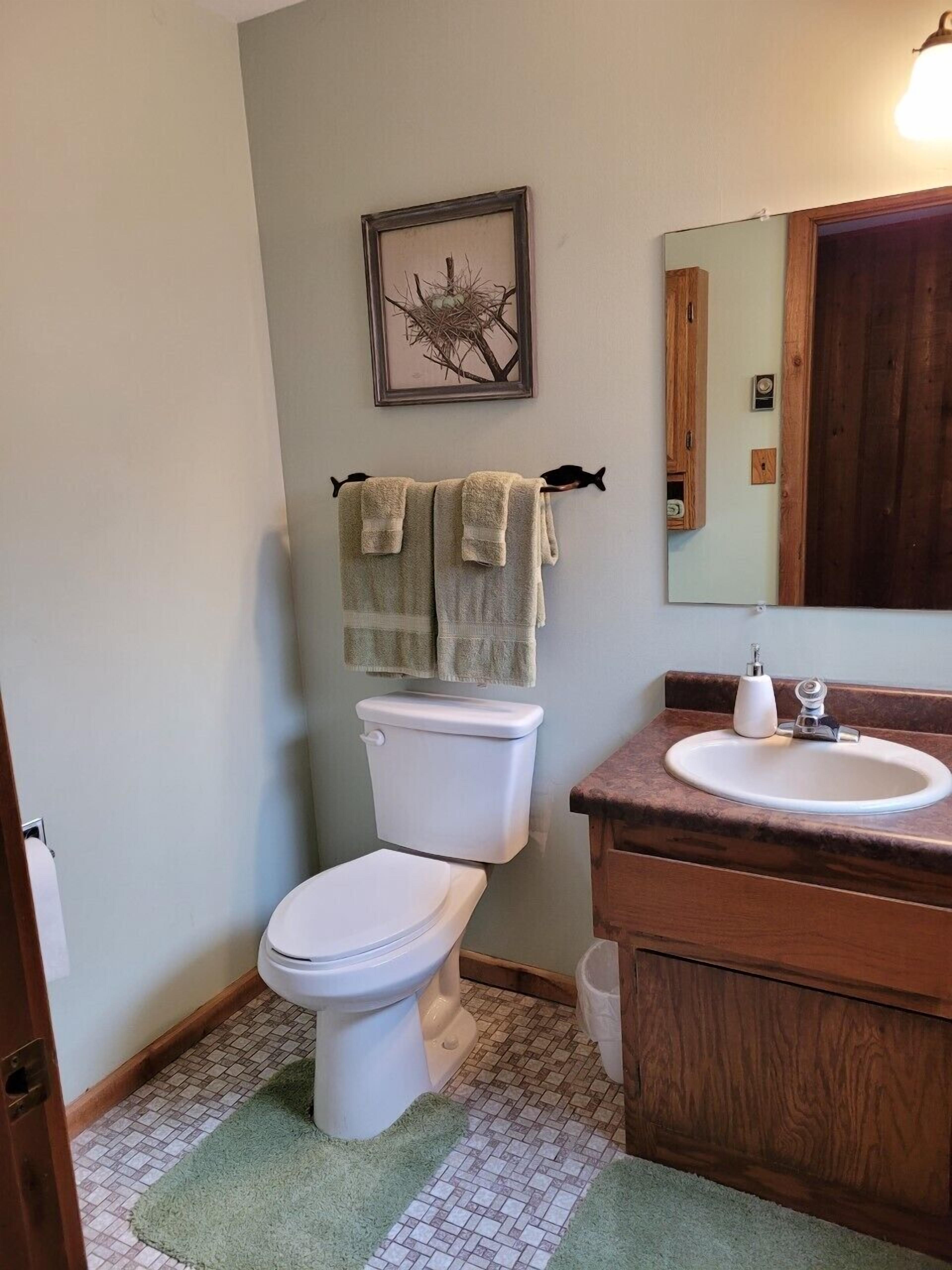 A bathroom with a toilet, sink, and a framed picture on the wall.