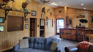 A wooden interior with a bar area, a sofa, and various mounted animal heads. - The Lodge (Cable)