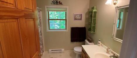 Un baño con puerta de madera, ventana, inodoro, lavamanos y espejo.